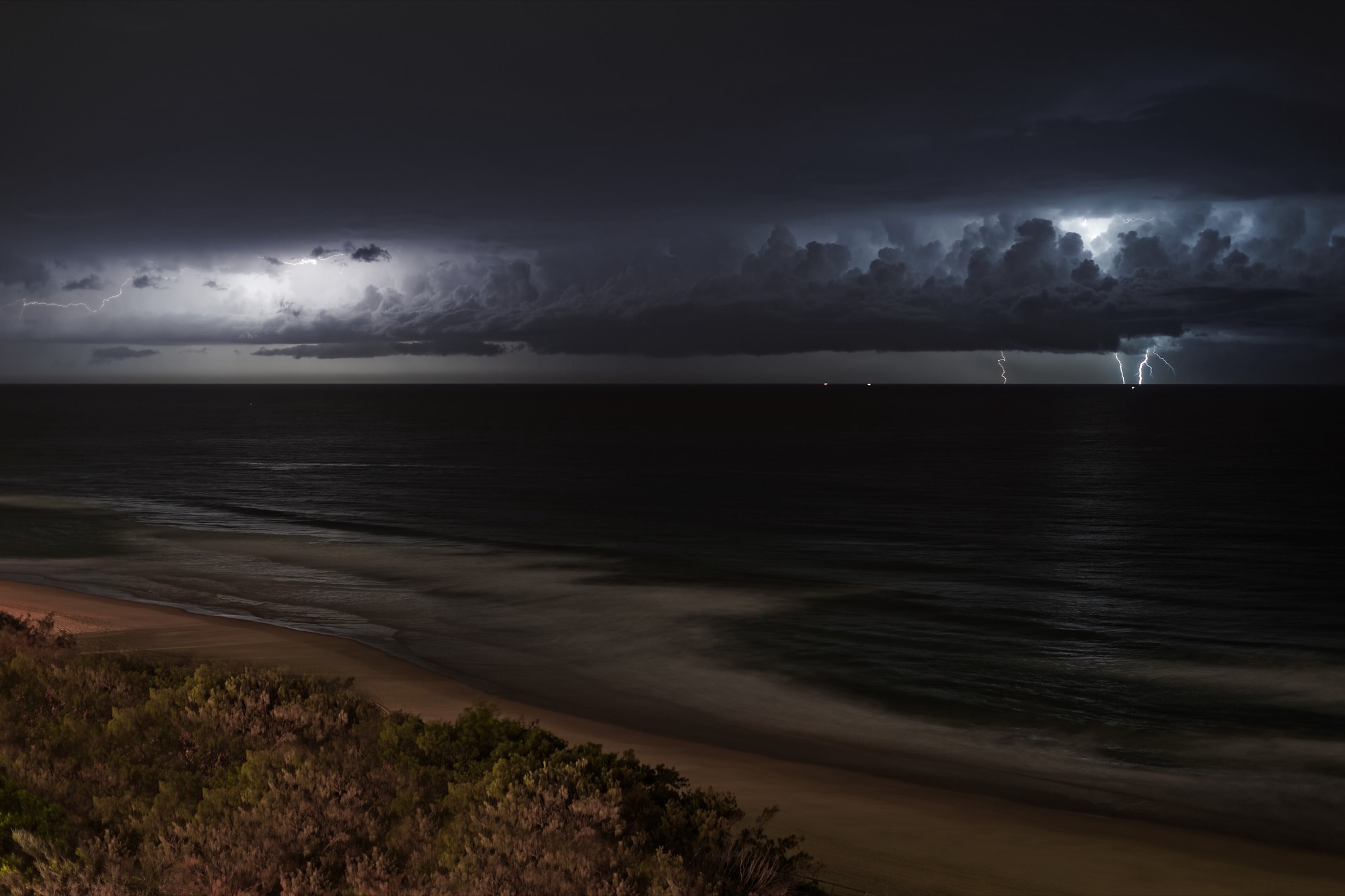 A dramatic storm over the dark ocean with powerful lightning striking the water.